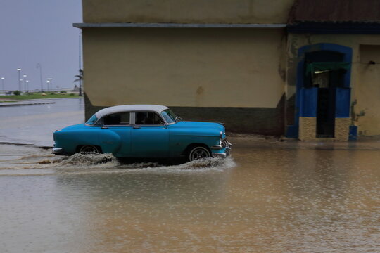 Blue almendron car -Chevrolet classic from 1954- drives up Marina Street wading a deep puddle in the heavy rain of a tropical storm. Havana-Cuba-127