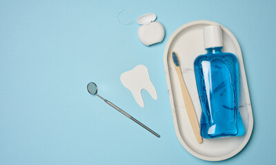 Mouthwash, toothpaste tube, dental floss and medical mirror on a blue background