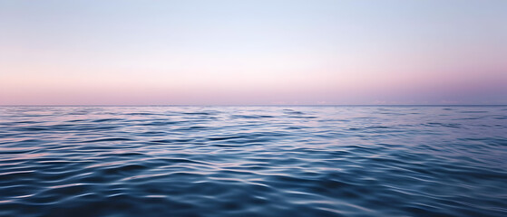 The calm sea merges with a pastel pink and blue sky at dawn, creating a peaceful scenery