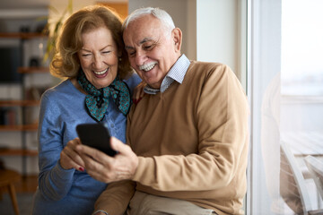 Happy mature couple talking while using mobile phone at home