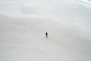 Minimalistic photo of person in black walking along white sand beach