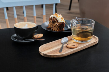 Delicious carrot cake with coffee and cup of tea next to it on wooden table. Cup of cappuccino and tea, slice of carrot pie with walnuts on black table.