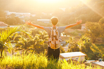 A young man with arms wide open atop a hill, with the sunset light in the background. It represents...