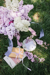 A greeting card with the inscription "Bonjour" lies on the grass, near a bouquet of purple, white and soft blue lilac and a purple silk ribbon. Decor © Olga