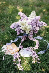 A greeting card with the inscription "Bonjour" lies on the grass, near a bouquet of purple, white and soft blue lilac and a purple silk ribbon. Decor © Olga