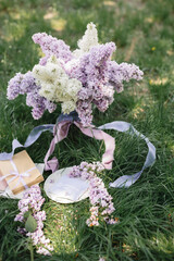 A greeting card with the inscription "Bonjour" lies on the grass, near a bouquet of purple, white and soft blue lilac and a purple silk ribbon. Decor © Olga