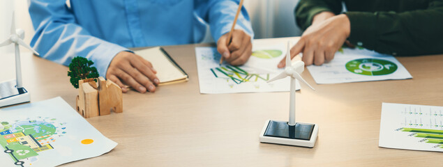 Fototapeta na wymiar Business people invest in green business plan at meeting room on table with house model and wind mill placed represented eco house and renewable energy. Closeup. Delineation.