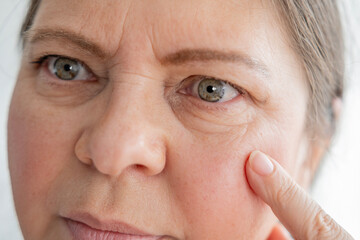 close up part of mature female face, woman 50-55 years old looks carefully examines wrinkles around...