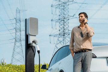 Man talking on the phone while recharge EV car battery at charging station connected to power grid...