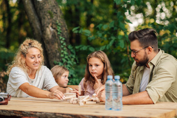 Parents making tower of wooden blocks while sitting with daughters in nature
