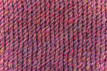 A close up of a knitted fabric with a variety of colors. The yarn is knotted and the fabric is purple