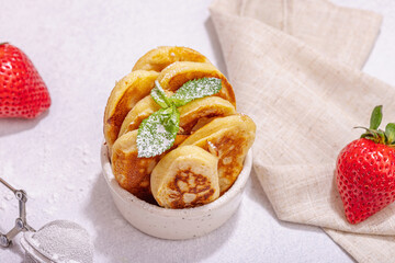 Cottage cheese pancakes, syrniki, curd fritters with strawberry, mint and powdered sugar in a bowl
