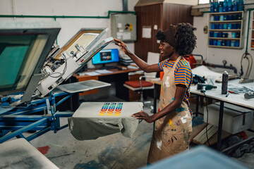 Interracial female printing shop worker finishing silk screen printing