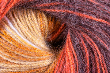 A close up of a skein of yarn with orange and brown colors. The yarn is twisted and has a spiral shape