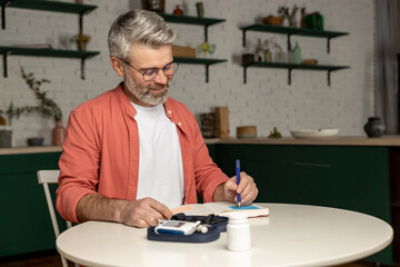Diabetic man checking level of sugar in blood with glucometer takes notes with indicators in notepad