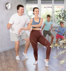 Joyous middle-aged parents engaged in dance in pairs together with their little children