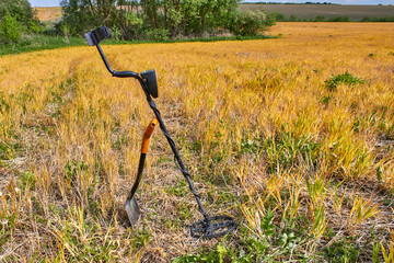 Metal detector for searching coins and jewelry and a metal shovel on a background of a yellow field. Treasure finding tools