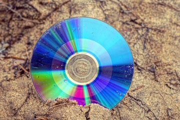 one old dirty colored compact disc lies on the brown ground in the street