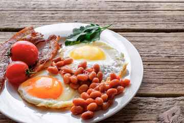 Full english breakfast with eggs, bacon, beans, tomatoes in a plate with fork on rustic wooden table. Tasty food