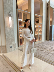 beautiful sensual woman with dark hair in luxurious white clothes with accessories posing in elegant lobby hotel