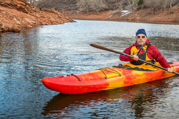 senior male paddler is paddling colorful river kayak on a calm lake  - recreation concept, cold season on Horsetooth Reservoir in Colorado