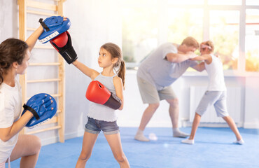 Mother and girl are engaged during training, boxing classes. Parent helps daughter master basic...