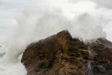 Obraz premium Immense waves hitting a large rock at the edge of the beach. Force of nature.
