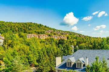 Lush greenery envelopes Mont Tremblant's residential area, with charming houses perched on the hillside under a clear blue sky, capturing the essence of the beautiful national park. Quebec, Canada
