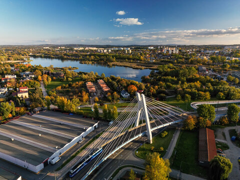 Drone panoramic sunset photo of city architecture and modern bridge in Krakow, Poland. Perspective overhead scenery view of high suspension bridge for transportation, Bagry bay with park around