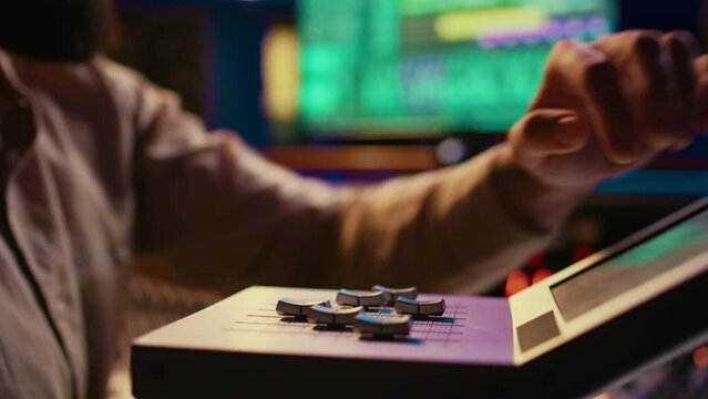 Sound engineer operating on motorized faders controller in professional studio, editing and mixing tracks to create a song. Audio technician works with sliders and soundboard panel. Camera B.