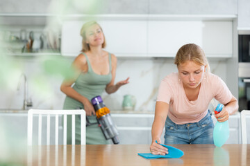 Teenage girl actively participating in household chores by assisting mother in cleaning apartment,...