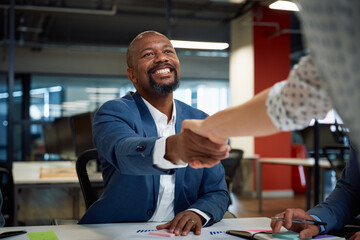 Three multiracial business people smiling while shaking hands during meeting in office - Powered by Adobe