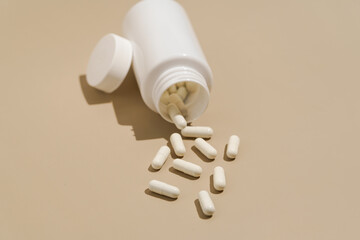 white capsule pills pouring out of a plastic jar on a beige isolated background. Concept of...