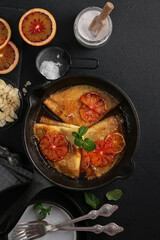 crepes suzette, delicious pancakes with orange sauce in the back pan on dark background, top view