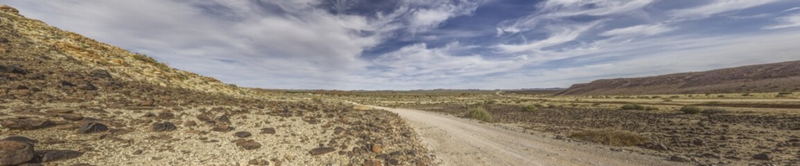 Fototapeta na wymiar Panoramic picture over a gravel road through the desert like steppe in southern Namibia under a blue sky