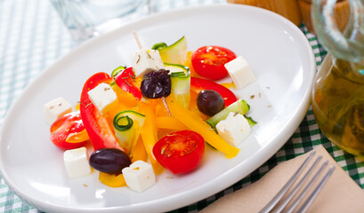 Fresh colorful Greek salad (horiatiki salad) served with feta cheese on white plate..