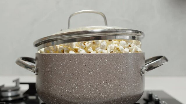 A whole pot of popcorn is being prepared on the gas stove, with so much that the lid rises above the ready kernels.
