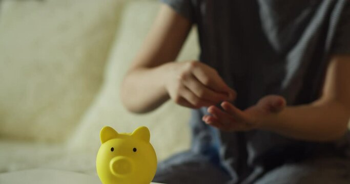 Child recounts his money and puts it in piggy bank. Schoolgirl throws coins into a yellow piggy bank. Coins in piggy bank symbol of banking security. Financial savings. Children in financial security.