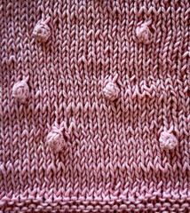 Background texture of a pink knitted baby blanket with baubles