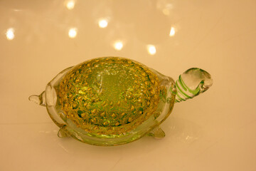A delicate glass turtle sculpture infused with sparkling gold flakes, captured against a reflective...