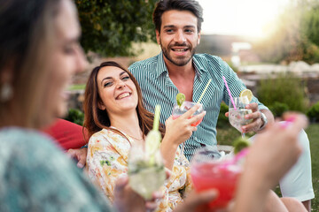 A group of friends cheerfully toasting with colorful cocktails in a garden setting, capturing the essence of a relaxed casual outdoor celebration - Joyful people having fun sharing drinks