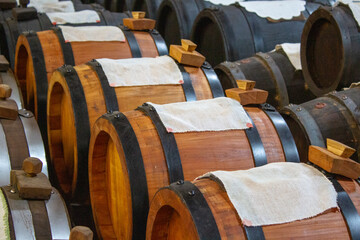 Neatly aligned oak barrels for aging olive oil, each topped with cloth, illustrating the...