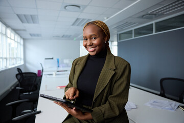 Confident young black businesswoman in businesswear using digital tablet by desk in office - 772626793