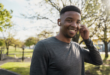 Young black man in sportswear listening to music with wireless earphones and smiling in park - 772630348