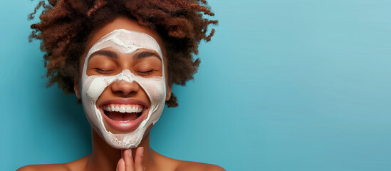 A woman's cheerful face is covered with a white facial mask, her eyes squinting with a big smile, against a teal background. - obrazy, fototapety, plakaty