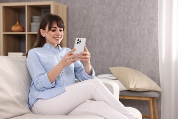 Beautiful young housewife using smartphone on sofa at home
