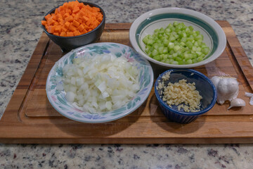 side view of chopped carrots, celery, onions and garlic in bowls with whole garlic on cutting board with copy space