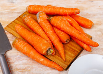 Fresh organic carrots on a wooden cutting kitchen board with kitchen knife