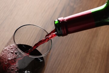 Pouring tasty red wine in glass at wooden table, closeup