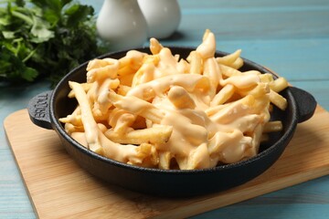 Delicious french fries with cheese sauce in bowl on light blue wooden table, closeup